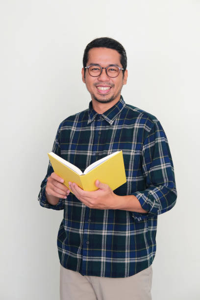 istock Adult Asian man smiling at the camera while holding a book 1448524416