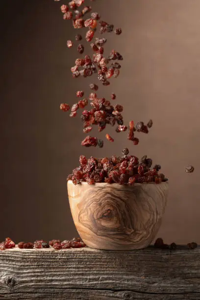 Flying raisins on a brown background. Raisins in a wooden bowl. Copy space.