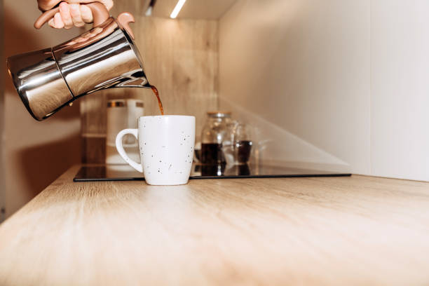 istock A woman's hand pours black coffee from a geyser coffee maker into a white mug, kitchen interior. Selective focus 1448532626