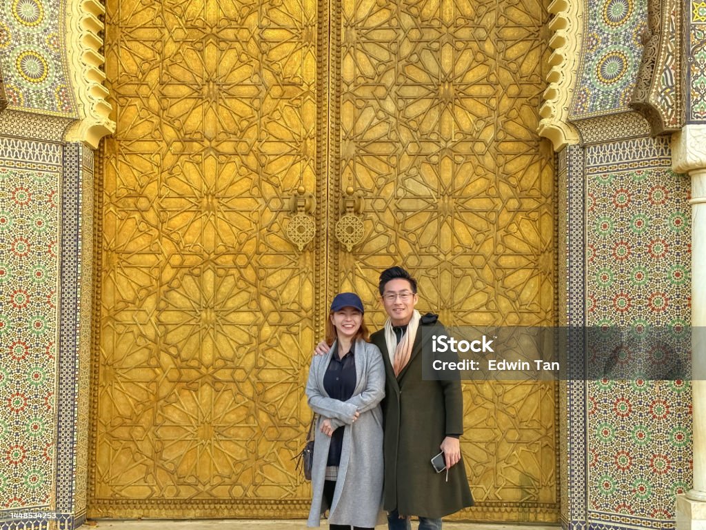 Asian Chinese tourist couple looking at camera standing atRoyal palace entrance in Fes, Morocco. Gilded Stock Photo