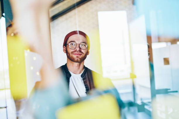 istock Handsome caucasian male designer in trendy eyewear thinking about ideas and solution of project looking at colorful stickers, 20s smart creative male student enjoying working process in office 1448535565