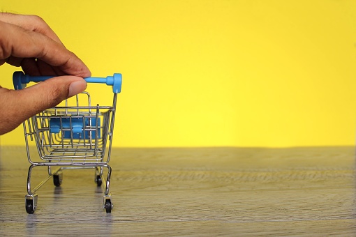 Hand push mini shopping trolley on yellow background with copy space. Shopping and consumer concept