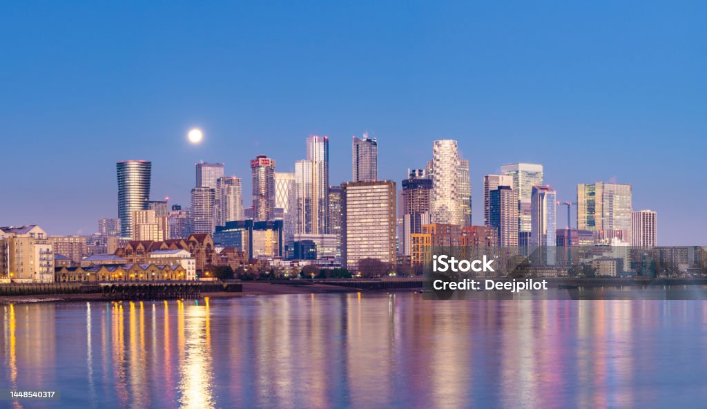 The London Canary Wharf City Skyline at Twilight, United Kingdom Setting Moon and Reflection in the Still River Thames, Copy Space City of London Stock Photo