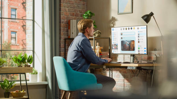 Young Handsome Man Using Desktop Personal Computer to Check Social Media Wall Feed, Live Stream Videos, Posts, Pictures. Mock-up Posts: Creativity, Tech, News, Science, Lifestyle Content.