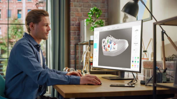 istock Young Male Footwear Designer Works on 3d Model of Shoe and Change Colours on It While Working on Desktop Computer in Creative Space. Shoe Production Procedure Concept. 1448542607