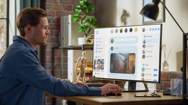 istock Young Handsome Man Using Desktop Personal Computer to Check Social Media Wall Feed, Live Stream Videos, Posts, Pictures. Mock-up Posts: Creativity, Tech, News, Science, Lifestyle Content. 1448542675