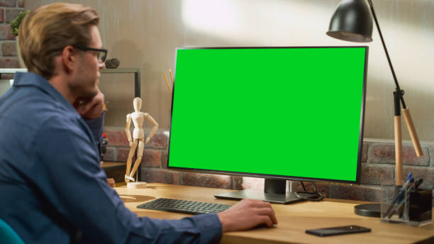 istock Young Handsome Man Working from Home on Desktop Computer with Green Screen Mock Up Display. Creative Male Checking Social Media, Browsing Internet. Living Room in Bright Loft Apartment. 1448542938