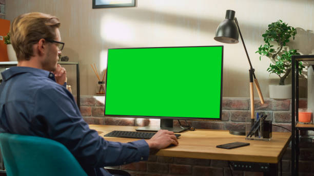 istock Young Handsome Man Working from Home on Desktop Computer with Green Screen Mock Up Display. Creative Male Checking Social Media, Browsing Internet. Living Room in Bright Loft Apartment. 1448543644