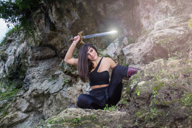 Beautiful warrior girl with sword in hand hidden among rocks - warrior woman concept