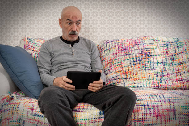 老人はソファに座って、タブレットコンピューターを見て非常に驚いた。 - ipad senior adult 70s adult ストックフォトと画像