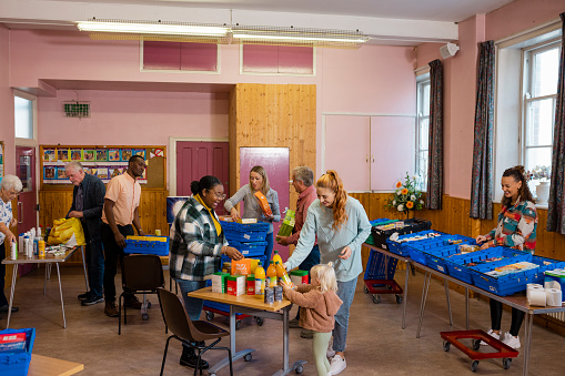 Food bank being run by volunteers at a community church in the North East of England. Mixed age and ethnic people in need are collecting groceries/toiletries there, including senior adults and a single mother with her young daughter.