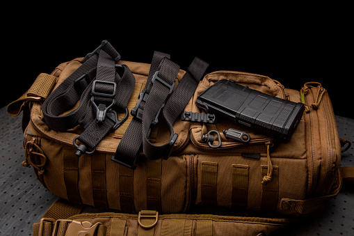 A black nylon weapon belt on a brown military backpack. Dark background.