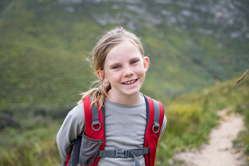 A portrait of a young girl enjoying nature. She is on a hike with a backpack