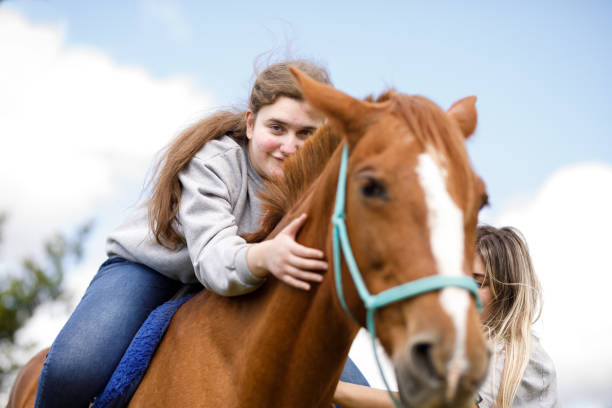 istock Girl during therapy with horses caressing a horse's neck while sitting on it's back 1448548287