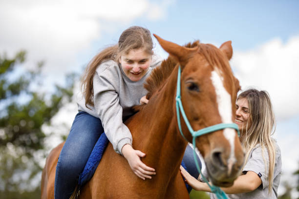 Girl learning how to caress a horse's neck while sitting on it's back during equine assisted therapy