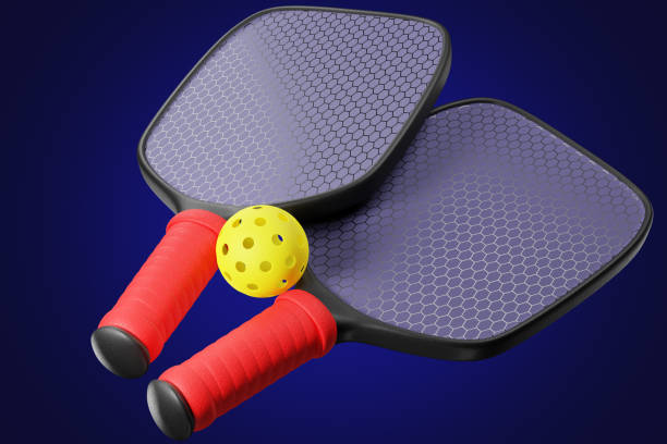 istock A ball with holes for a pickleball and two paddle rackets on a blue background. 3d rendering 1448549419