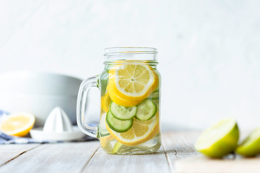 Bottle of infused water on white wood with lemon and  cucumber slices.