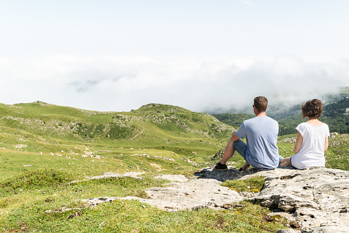 Young couple sitting at the top of a hill and looking at view in french Pyrenees.