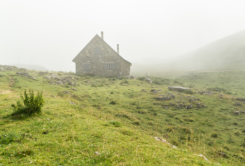 Stone cottage on a green hill at a foggy morning.