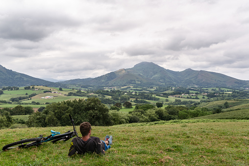 Cyclist lying down, resting on top of a green hill and looking at a beautiful mountainous landscape. Pyrenees, Spain