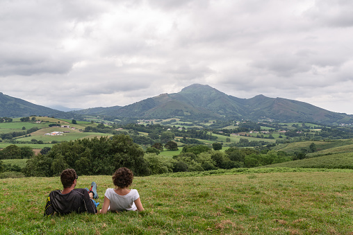 Young couple resting on top of a green hill and looking at a beautiful mountainous landscape. Pyrenees, Spain.