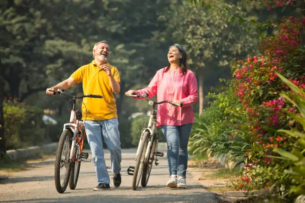 Photo of Cheerful senior couple laughing and walking with bicycles in park