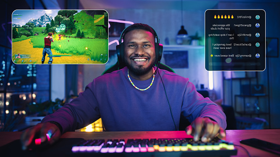 Excited African American Streamer Playing a Shooter Video Game. Man Streaming His Gaming Progress from Home in Living Room Apartment. Followers Engaging Through Interface, Live on Internet.