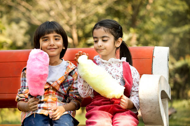 istock Cute siblings eating cotton candies while sitting in park 1448556259