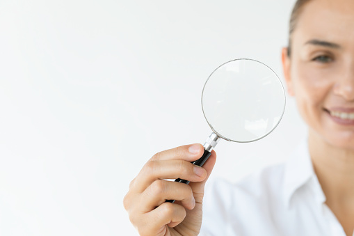 Smiling businesswoman is showing magnifying glass to camera. Representing business strategy , retrospective, analysis , research and solution concept.