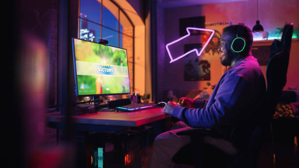 istock Successful Black Gamer Playing and Winning in PvP Shooter Video Game in Which Competitors Fight in a Battle Royale Tournament on Personal Computer. Stylish Man Celebrating Victory in Cozy Room at Home 1448558342