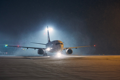 Winter night at airport. Airplane taxiing to runway for take off during heavy snowfall.