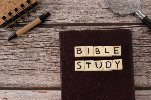 Bible study text written on wooden cubes, Christian holy book, notebook, magnifying glass, and pen on wooden background. Top table view. Searching and exploring Scriptures concept.