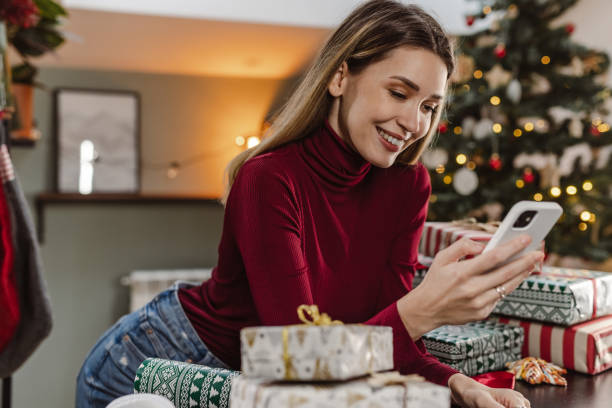 istock Beautiful young woman using smart phone during Christmas time at home 1448570877