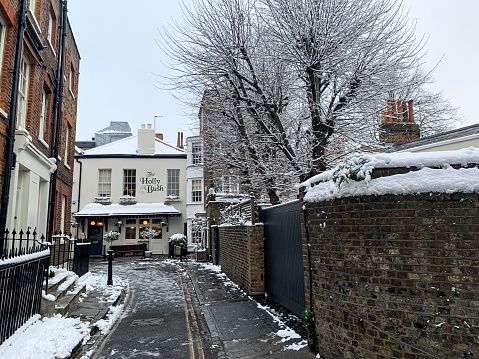 View of cozy famous pub located in Hampstead, Holy Mount street. Charming pub facade, yellow building with Christmas decoration. Winter in London. Snow in Hampstead. Snowing.
