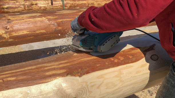 istock Worker grinds a log with an electric tool. Preparation for building a house. 1448579324