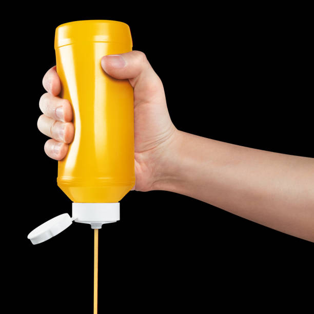istock Hand squeezing mustard out of a plastic bottle on black 1448579513