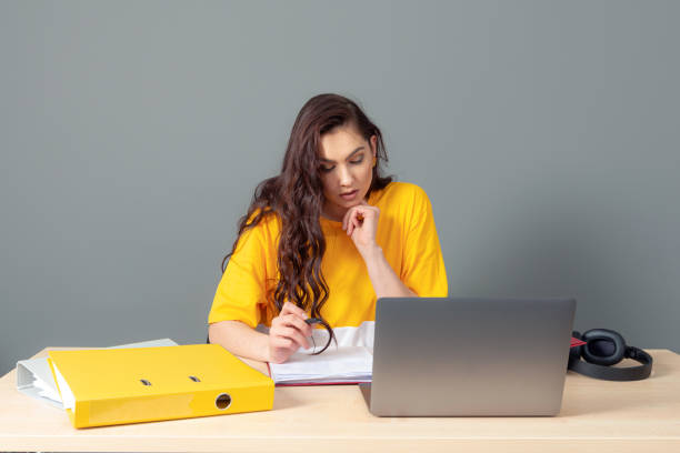 jeune femme d’affaires avec le long cheveu foncé travaillant avec le document dans le bureau, isolé sur le fond gris - paper document pen long hair photos et images de collection