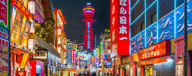 The iconic spire of the Tsutenkaku Tower overlooking the colourful neon lights illuminating the bars and restaurants of Shinsekai at night in the heart of Osaka, Japan’s vibrant second city.