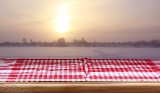 empty table with a red checkered tablecloth against the background of a winter sunset. layout, kitchen countertop, space for mounting your object.