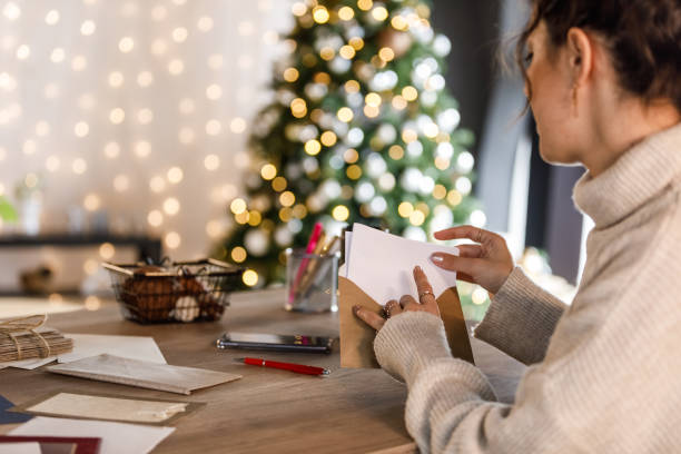 jovem mulher colocando a carta de natal que ela escreveu em um envelope - handwriting correspondence writing women - fotografias e filmes do acervo