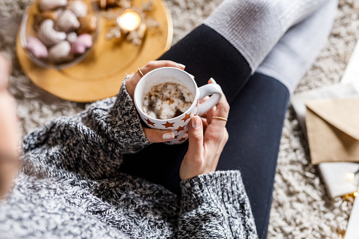 Directly above shot of unrecognizable young woman spending a cozy winter's day at home, she is sitting on the floor, relaxing and enjoying a cup of hot chocolate with marshmallows.