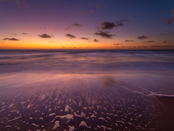 A seascape during sunset. Sand on the seashore. Bright sky during sunset. A sandy beach at low tide. Long exposure. Photo for wallpaper.