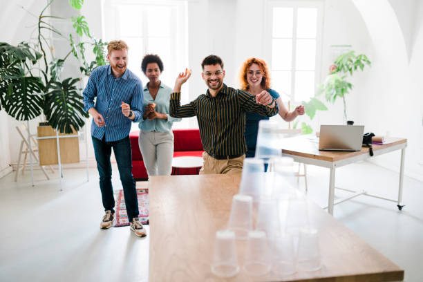 istock Business people having fun at the office, playing office games while on a break, tearing down a pyramid of plastic cups with a  ball 1448583817