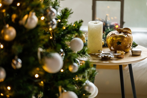 Close up shot of a small coffee table with various decorations arranged on it set up next to a glistening Christmas tree.