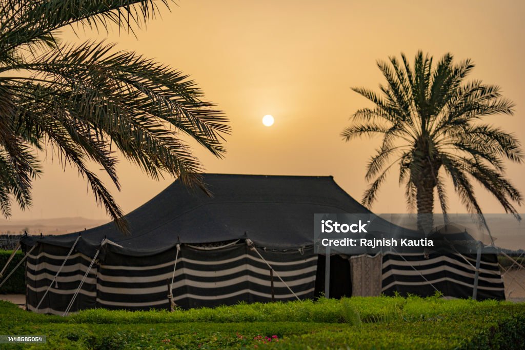 Sunrise in the Liwa Desert Early morning in the desert with the Traditional Arabic majlis tent and palm trees in the foreground. Abu Dhabi Stock Photo