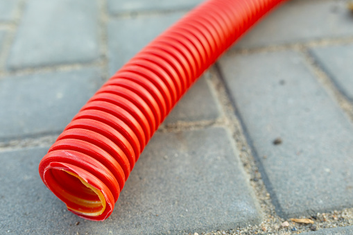 Red corrugated hose for electrical wiring on paving slabs. Close-up, selective focus