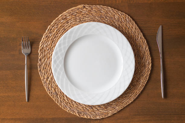 istock Empty white plate on a wicker supla with fork and knife on wooden table. Top view. 1448586194