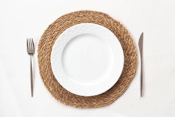 istock Empty white plate on a wicker supla with fork and knife on white table. Top view. 1448586218