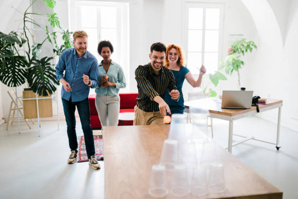 istock Business people having fun at the office, playing office games while on a break, tearing down a pyramid of plastic cups with a  ball 1448586484