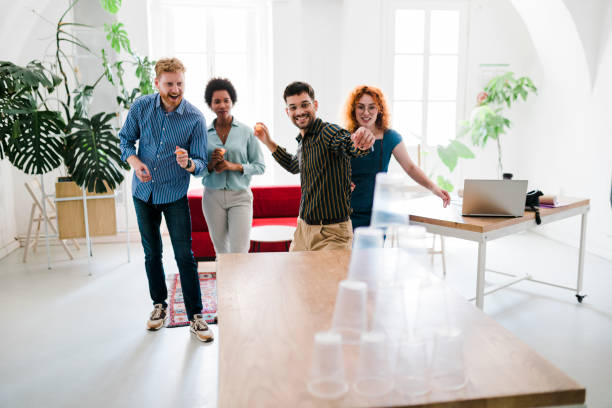 istock Business people having fun at the office, playing office games while on a break, tearing down a pyramid of plastic cups with a  ball 1448586546